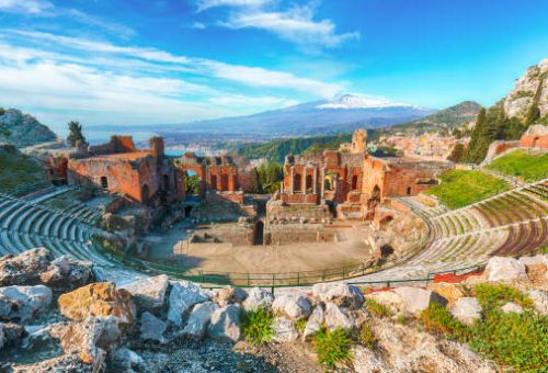 Ruins of ancient Greek theater in Taormina and Etna volcano in the background. Coast of Giardini-Naxos bay, Sicily, Italy, Europe.